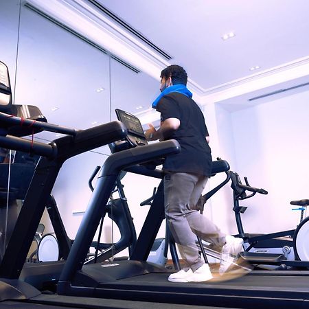 Makarem Ajyad Makkah Hotel Мекка Экстерьер фото The photo shows a person exercising on a treadmill in a modern gym or fitness room. The individual is wearing a blue neck support while jogging on the treadmill, which is set against a backdrop of large mirrors. There are also additional exercise equ