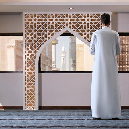 Makarem Ajyad Makkah Hotel Мекка Экстерьер фото The photo depicts a person standing with their back facing the viewer, wearing a traditional white garment. They are in a spacious interior setting that features an ornate archway with intricate patterns, typical of Islamic architecture. Through the 