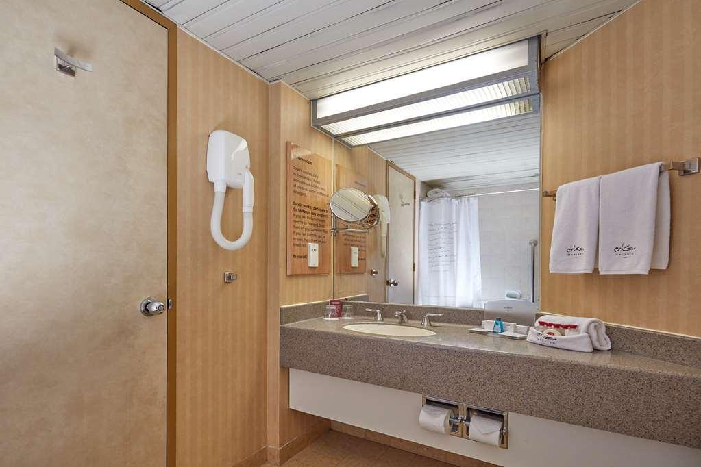Makarem Ajyad Makkah Hotel Мекка Экстерьер фото The photo shows the interior of a bathroom. It features a light-colored wall with vertical stripes and a ceiling that is white and textured. There is a gray countertop with a sink and a mirror above it. On one side, there are two white towels hanging