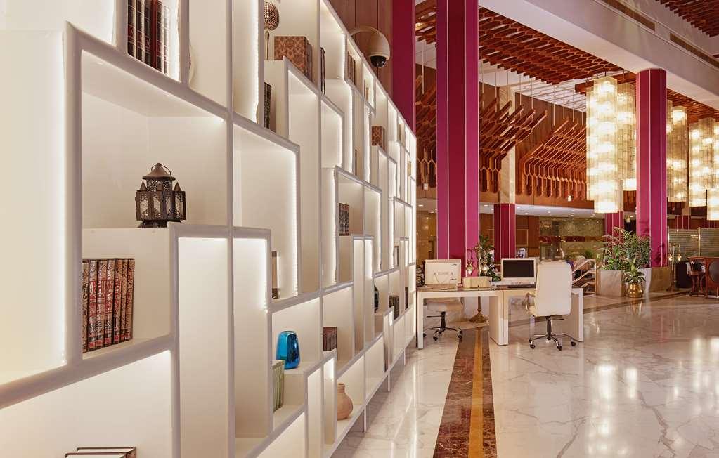 Makarem Ajyad Makkah Hotel Мекка Интерьер фото The photo shows a modern interior space, likely a lobby or lounge area of a stylish hotel or building. There is a partition wall made up of white shelving units illuminated from within, displaying various decorative items, books, and vases. The desig