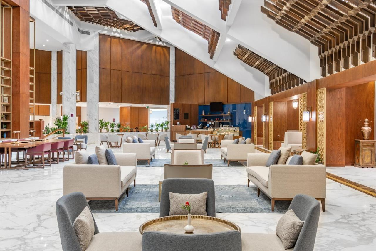 Makarem Ajyad Makkah Hotel Мекка Экстерьер фото The photo depicts the interior of a modern and elegantly designed lobby or lounge area. It features a spacious layout with high ceilings, showcasing a combination of wooden elements and marble flooring. 

In the center, there are several seating arra