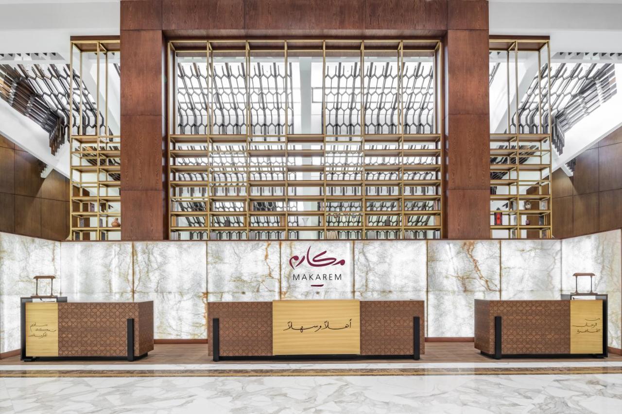 Makarem Ajyad Makkah Hotel Мекка Экстерьер фото The photo shows the interior of a hotel or a reception area, characterized by a modern and elegant design. In the foreground, there are multiple reception desks with a polished finish. Behind the desks, a striking feature is a wooden wall with a geom