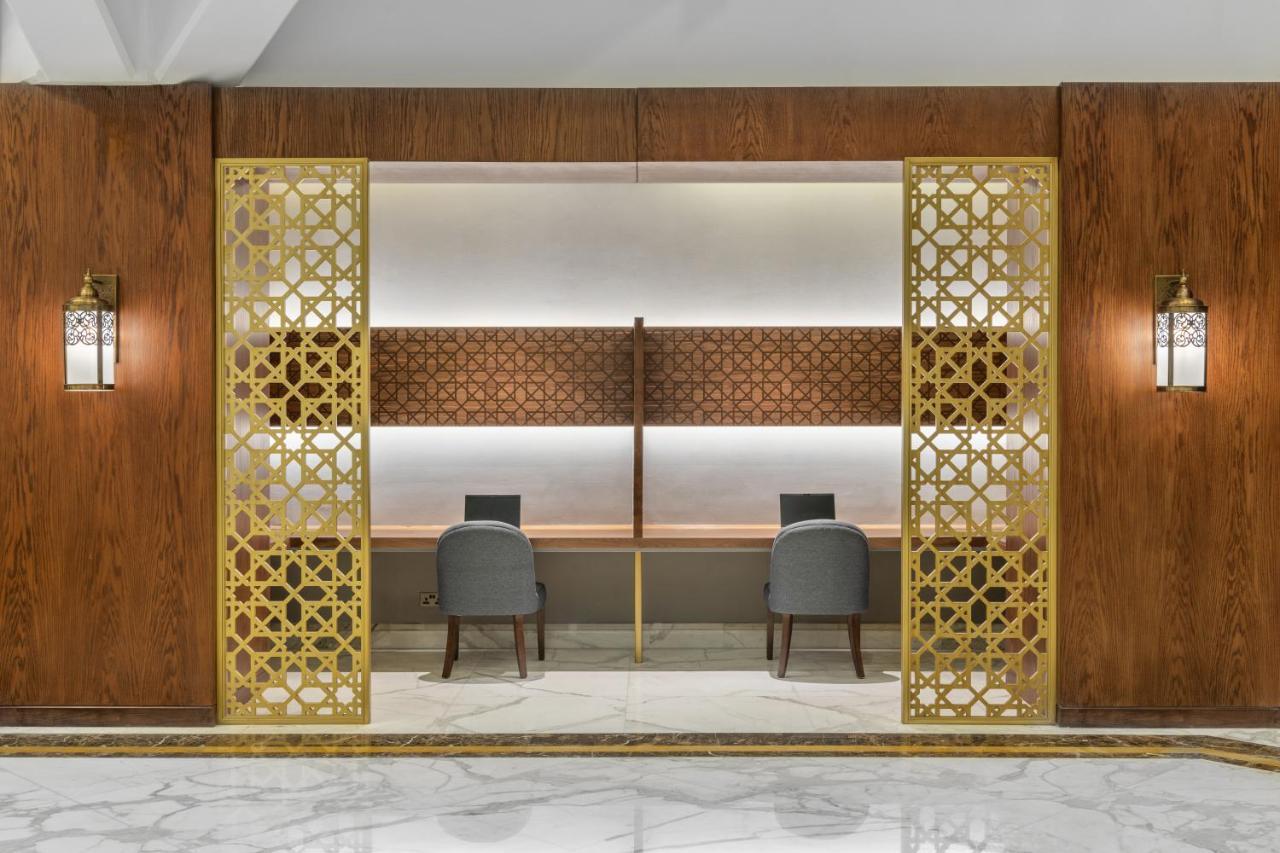 Makarem Ajyad Makkah Hotel Мекка Экстерьер фото The photo shows an elegantly designed space that features a reception or working area. There are two workstations with chairs positioned in front of them. The backdrop has a decorative panel with a geometric pattern. The area is framed by ornate gold