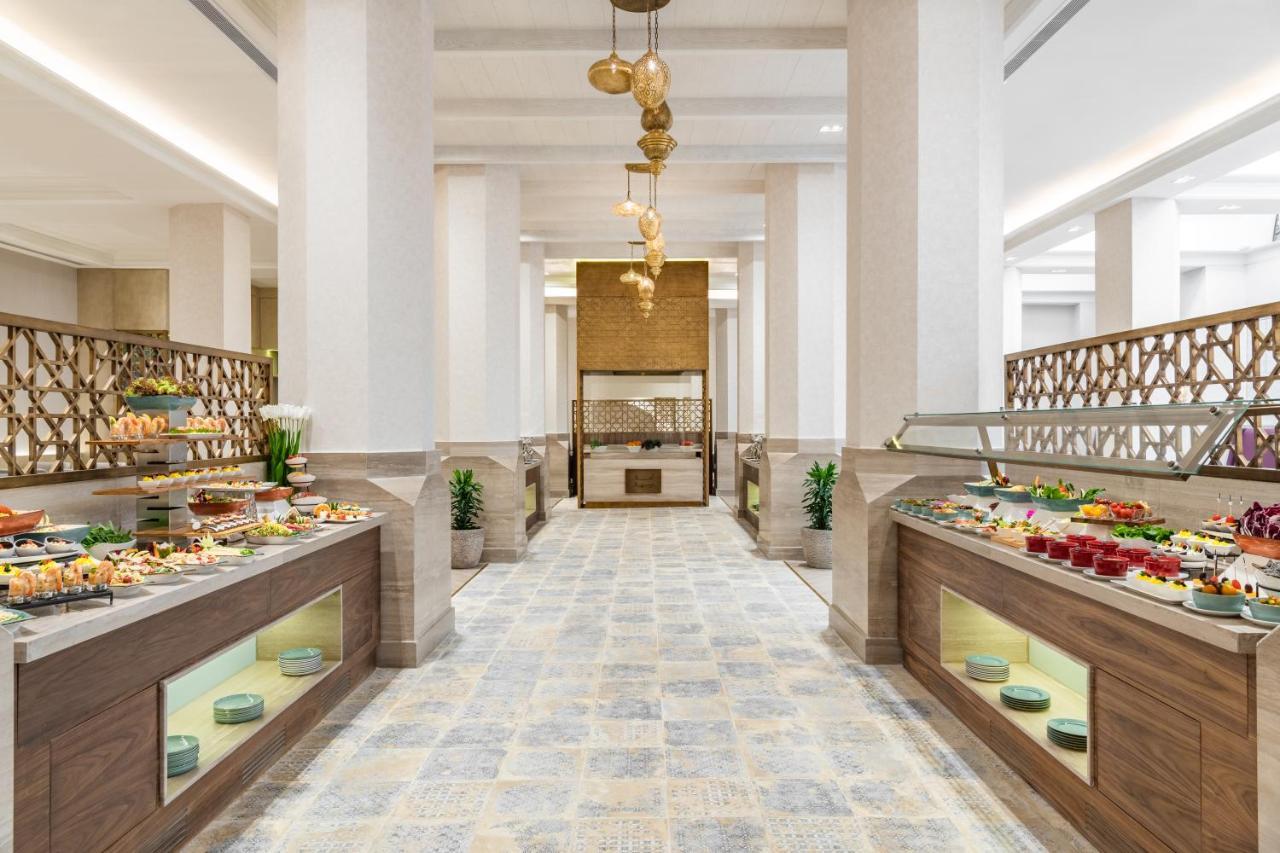 Makarem Ajyad Makkah Hotel Мекка Экстерьер фото The photo shows an elegant restaurant or buffet area. There are two long buffet tables on either side, displaying a variety of colorful dishes and desserts. The tables have an organized layout and are adorned with small plants. In the center of the r