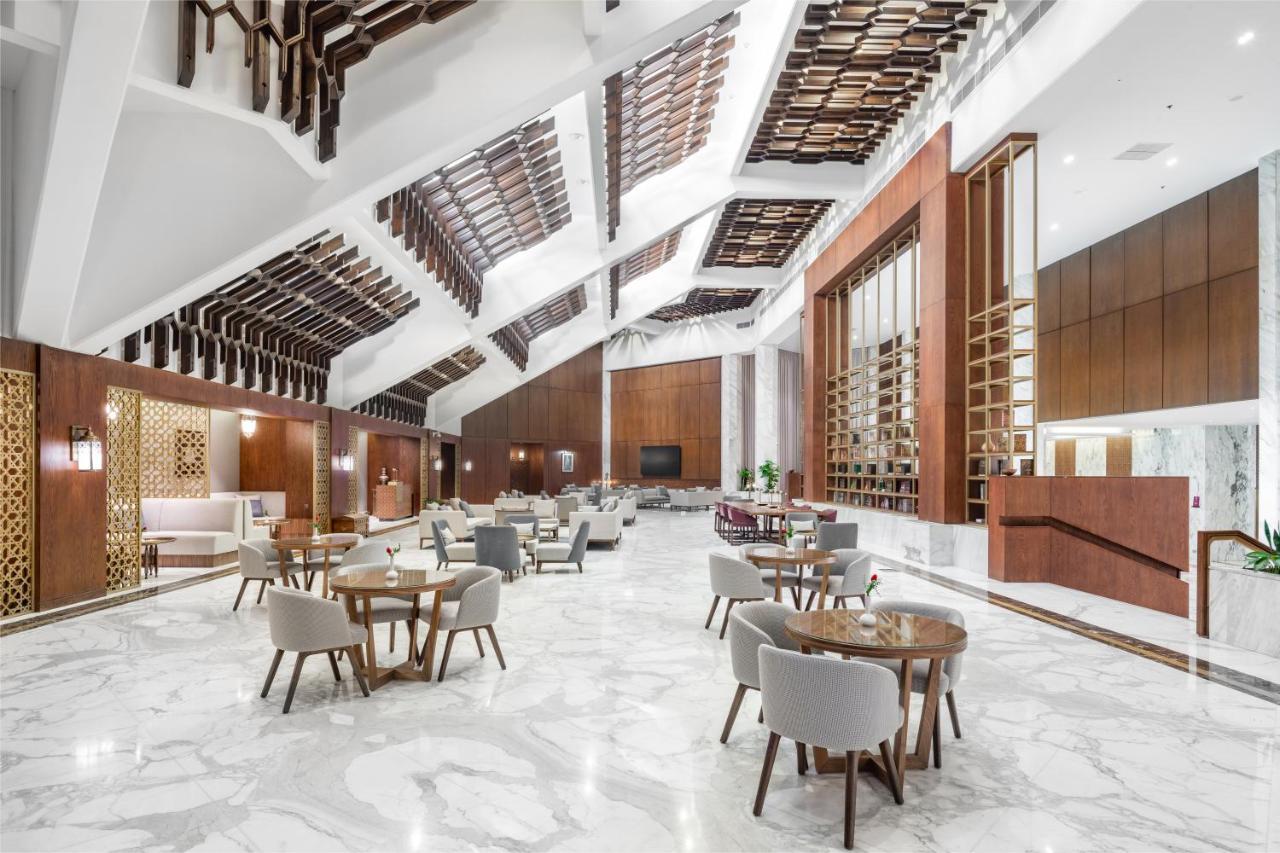 Makarem Ajyad Makkah Hotel Мекка Экстерьер фото The photo shows a spacious and modern interior, likely of a hotel or a large dining area. The design features high ceilings with an interesting architectural style, including a combination of wooden elements and sleek, modern finishes. 

The floor is