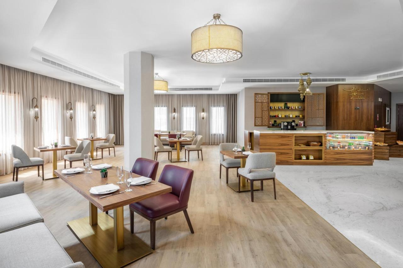 Makarem Ajyad Makkah Hotel Мекка Экстерьер фото The photo depicts a modern and stylish restaurant interior. The space features a combination of wooden and upholstered furniture, with several dining tables arranged throughout. The tables are set with dishes and cutlery, indicating readiness for ser