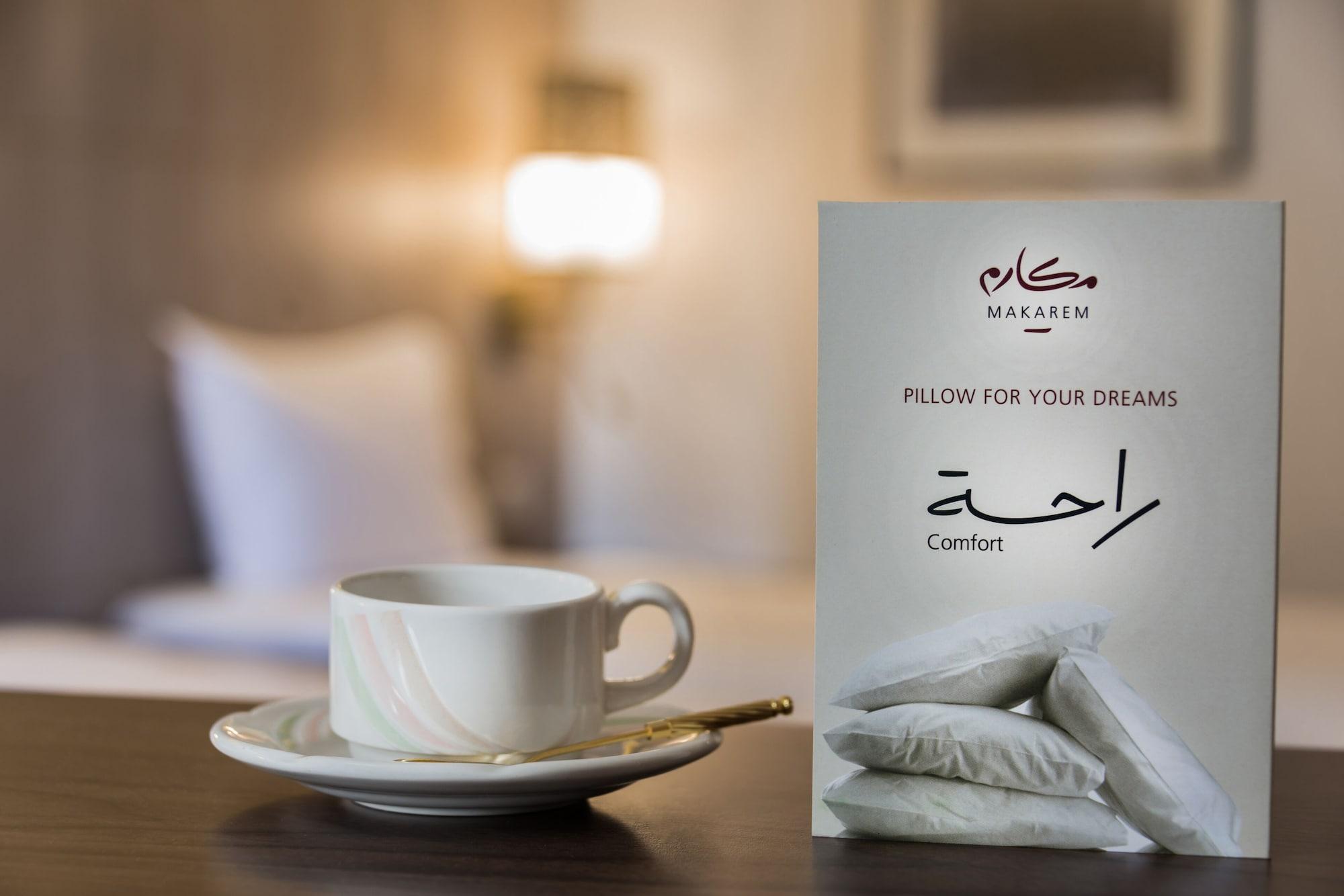 Makarem Ajyad Makkah Hotel Мекка Экстерьер фото The image features a cozy setting, likely a hotel room. In the foreground, there is a white cup of coffee or tea placed on a small saucer, accompanied by a gold spoon. Beside the cup is a decorative card or sign that reads "Pillow for Your Dreams" an