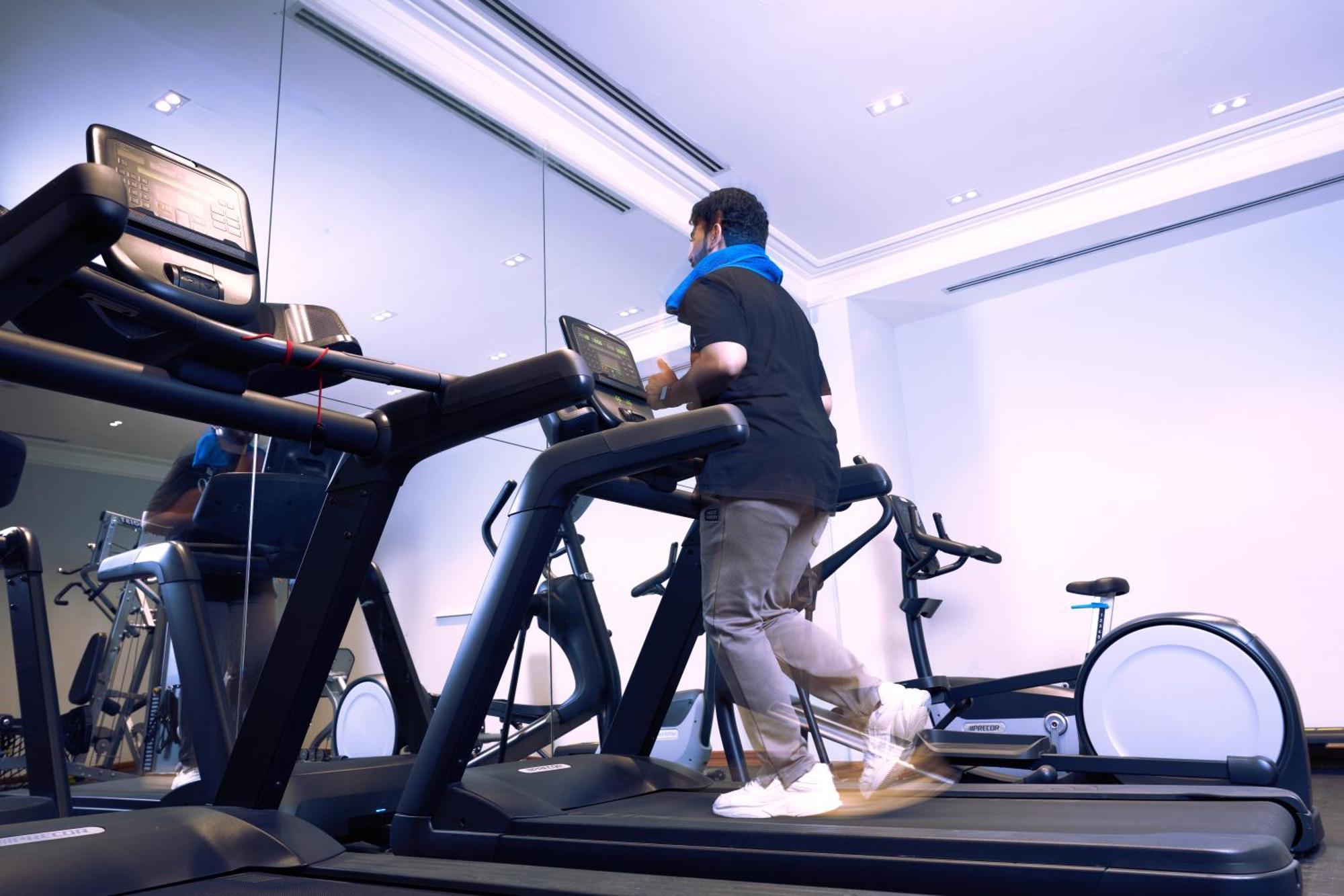 Makarem Ajyad Makkah Hotel Мекка Экстерьер фото The photo shows a person exercising on a treadmill in a modern gym or fitness room. The individual is wearing a blue neck support while jogging on the treadmill, which is set against a backdrop of large mirrors. There are also additional exercise equ