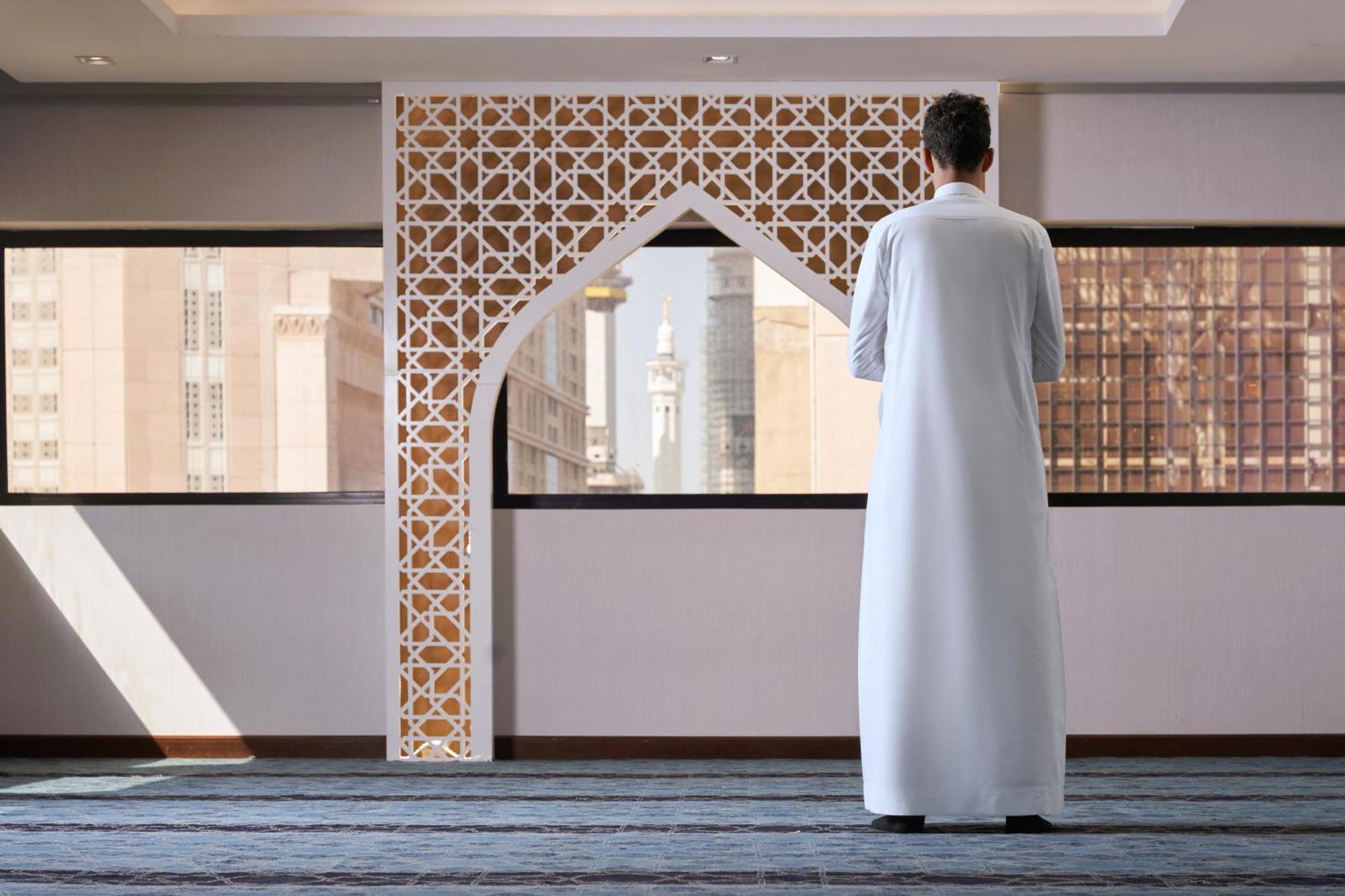 Makarem Ajyad Makkah Hotel Мекка Экстерьер фото The photo depicts a person standing with their back facing the viewer, wearing a traditional white garment. They are in a spacious interior setting that features an ornate archway with intricate patterns, typical of Islamic architecture. Through the 