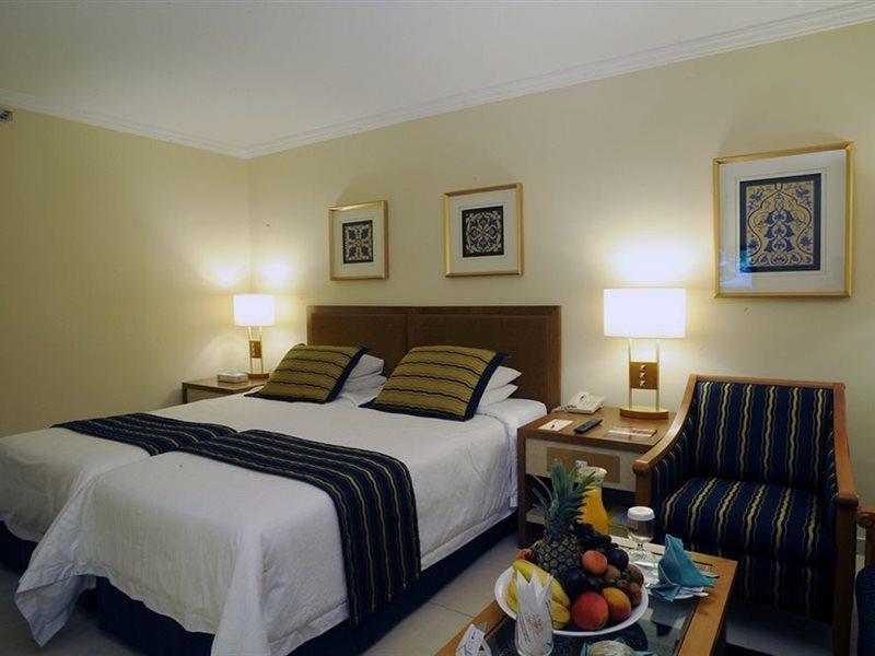 Makarem Ajyad Makkah Hotel Мекка Экстерьер фото The photo shows a hotel room with a cozy and inviting atmosphere. It features two beds with white linens and dark striped bedspreads. There are two bedside lamps providing warm light, and the walls are decorated with framed artworks. Beside the beds 
