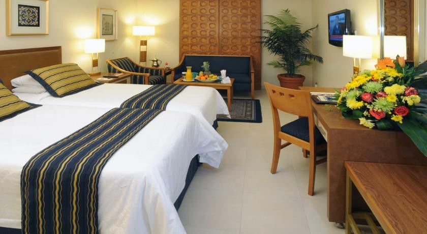 Makarem Ajyad Makkah Hotel Мекка Экстерьер фото The image shows a hotel room featuring two beds with white linens and a decorative stripe along the edge. There is a seating area with two chairs and a small table, set with a breakfast spread that includes fruit and drinks. A small potted plant adds