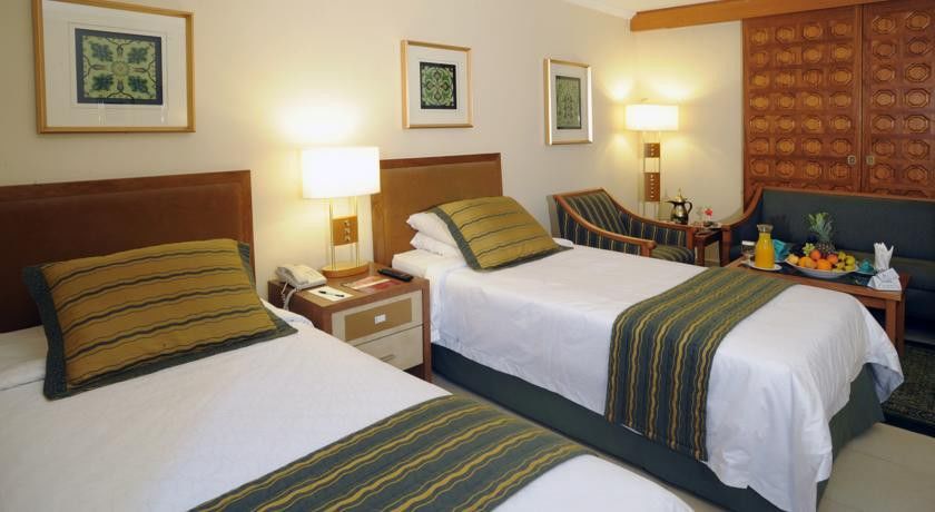 Makarem Ajyad Makkah Hotel Мекка Экстерьер фото The photo shows a hotel room with two twin beds, each topped with decorative green and gold striped bed runners. There is a nightstand between the beds with a lamp on it. The room features light-colored walls, framed artwork on the walls, and a small